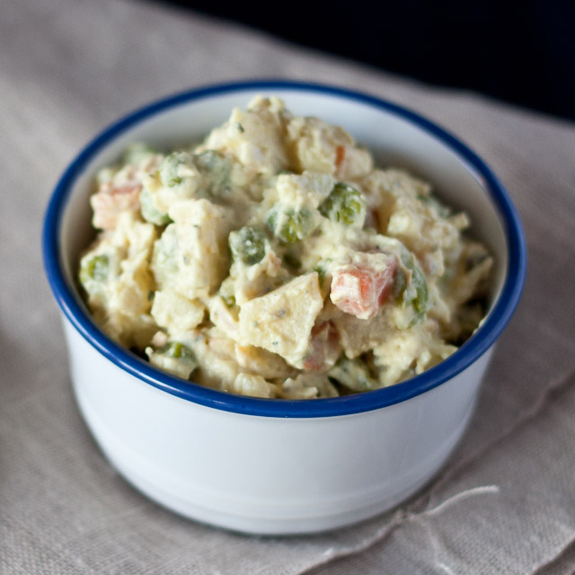 A bowl of creamy Polish vegetable salad (Sałatka Jarzynowa) with peas, diced carrots, and potatoes, garnished with herbs.