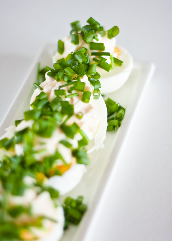 Polish eggs topped with mayo and chopped green onions, served on a white plate.