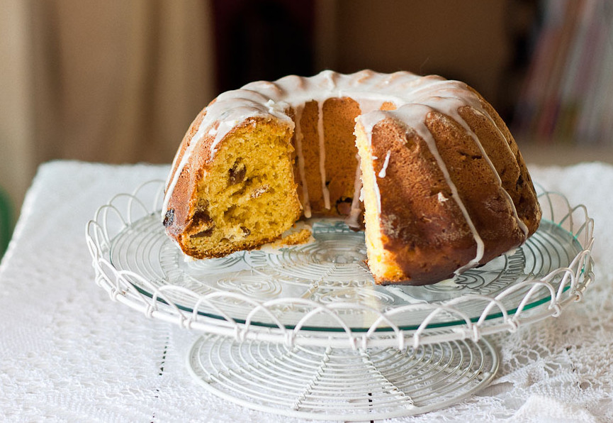 A partially sliced lemon bundt cake topped with a light icing, displayed on a decorative wire cake stand.