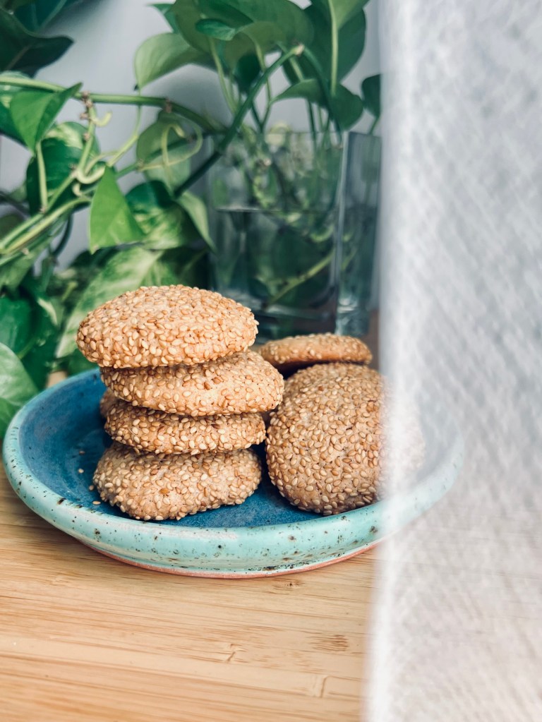 A stack of sesame cookies on a blue ceramic plate, surrounded by greenery in the background.