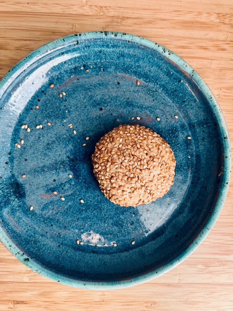 A single sesame cookie on a blue ceramic plate, showing a crispy texture and golden color.